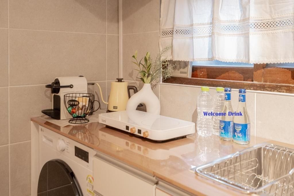 A kitchen with a coffee maker, a tea kettle, a vase with flowers, and a sink with a dish rack.