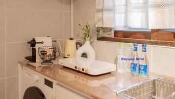 A kitchen with a coffee maker, a tea kettle, a vase with flowers, and a sink with a dish rack.