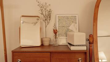 A wooden dresser with a mirror, a framed botanical print, a vase with dried flowers, and a tissue box.