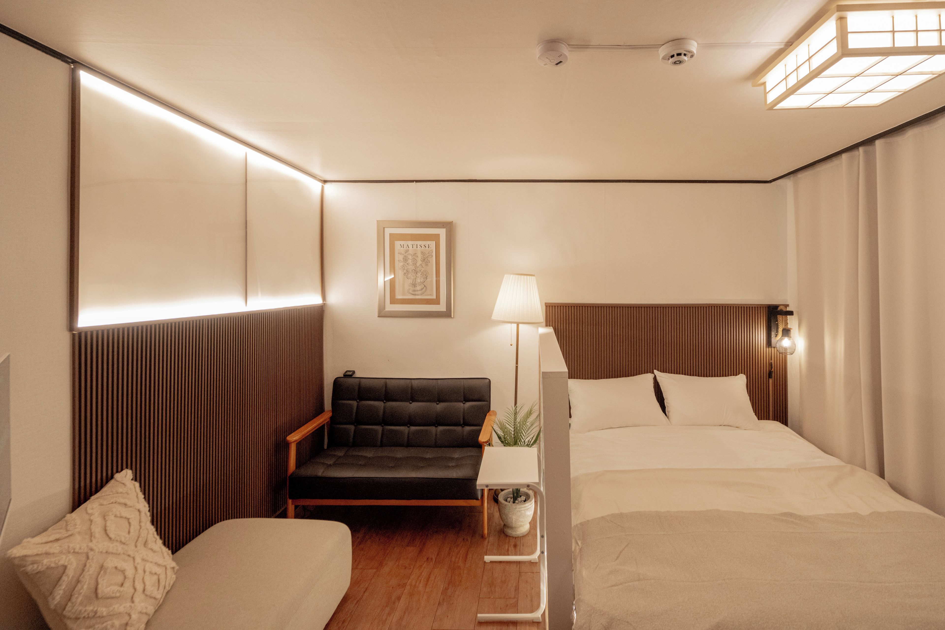 Una habitación de hotel con una cama, una silla, una mesita de noche, una lámpara y una obra de arte enmarcada en la pared.
