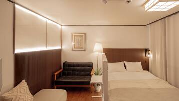 Una habitación de hotel con una cama, una silla, una mesita de noche, una lámpara y una obra de arte enmarcada en la pared.