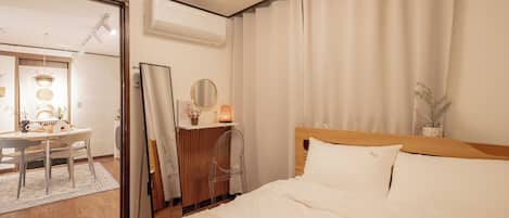 A hotel room with a bed, a desk, a mirror, and a window with curtains.