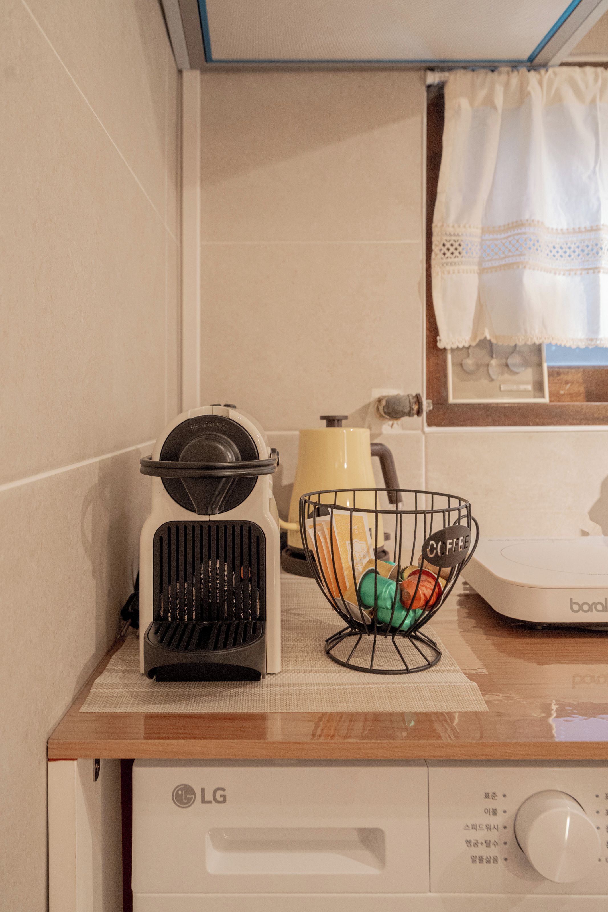 Una kitchenette con cafetera, una cesta de cápsulas de café y un microondas.