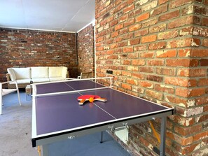 Ein Pingpongtisch, der an eine Ziegelwand gelehnt ist, mit einem weißen Sofa im Hintergrund.