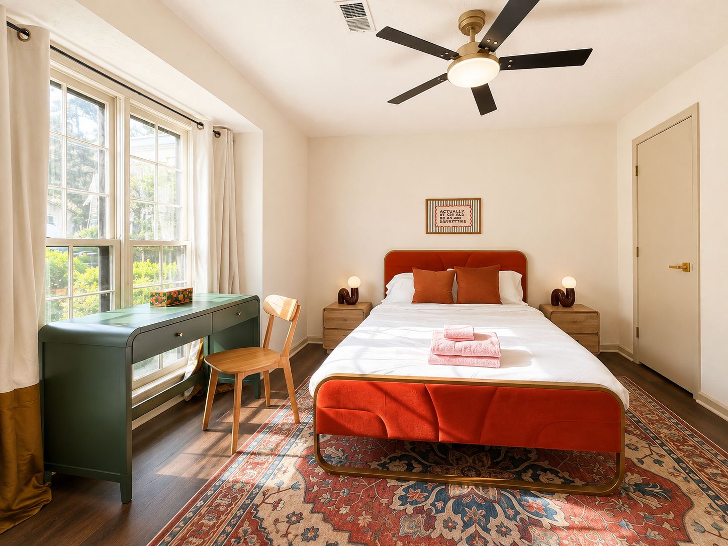 A bedroom with a bed, a desk, a chair, a ceiling fan, and a window.