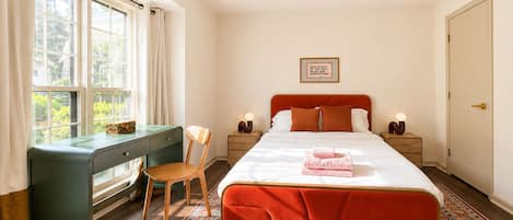 A bedroom with a bed, a desk, a chair, a ceiling fan, and a window.