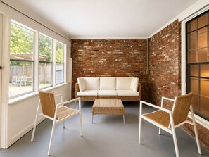 Ein Zimmer mit einer Ziegelwand, einem weißen Sofa und zwei Korbstühlen.