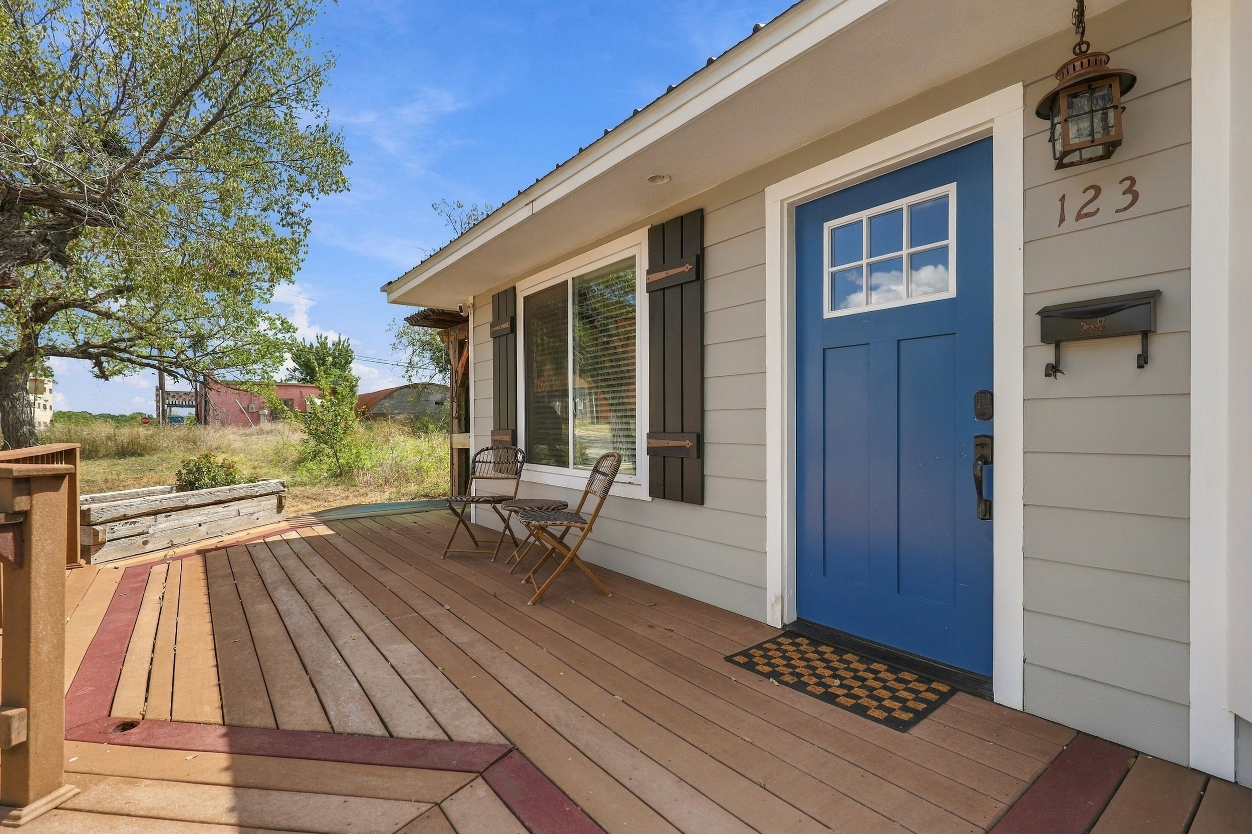 A house with a blue door, a porch with wooden flooring, and a number 123 on the wall.