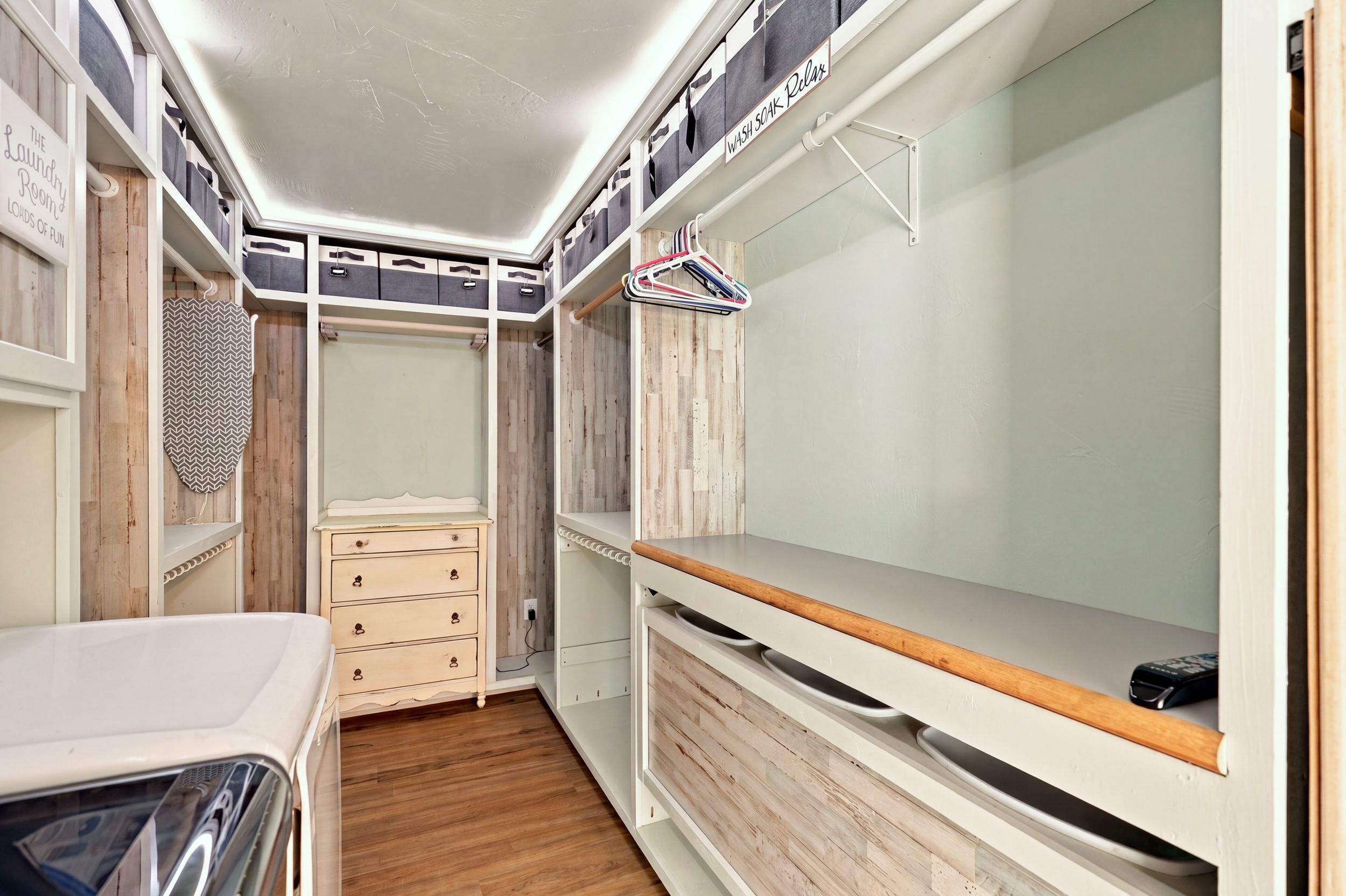 Une petite buanderie bien aménagée, avec des bacs de rangement, un étendoir et une petite commode.