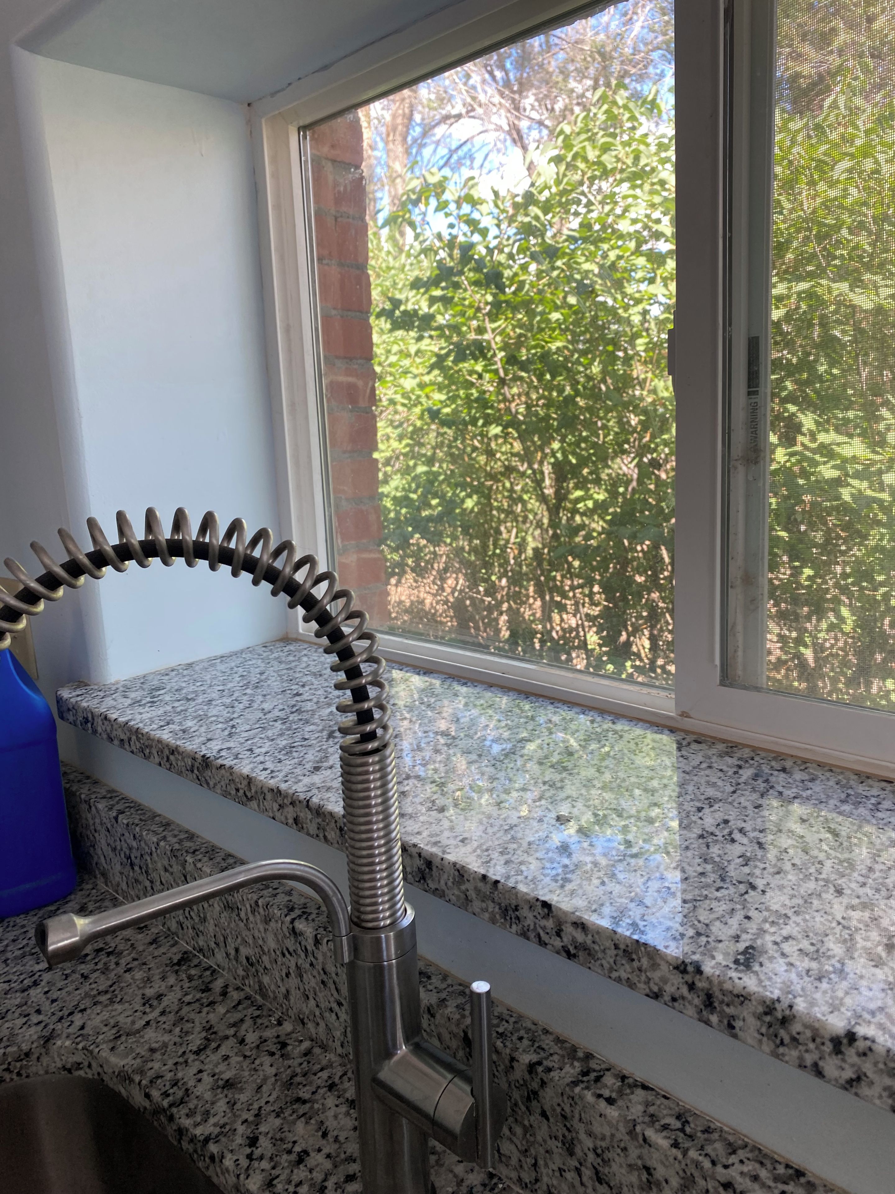Una cocina con encimeras de granito, un grifo de acero inoxidable y ventana con vista a la vegetación.