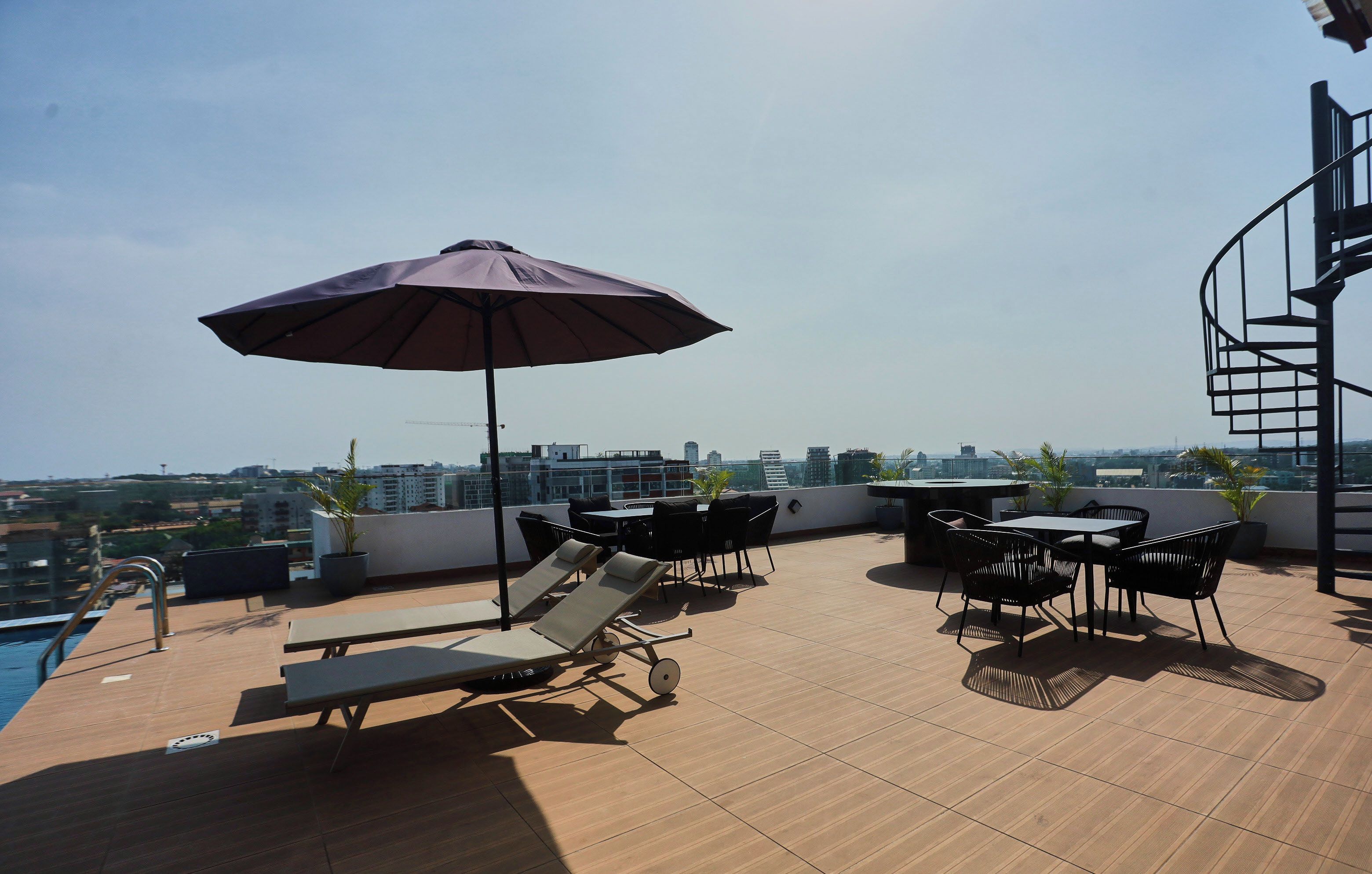 A rooftop terrace with a pool, lounge chairs, a table, and an umbrella.