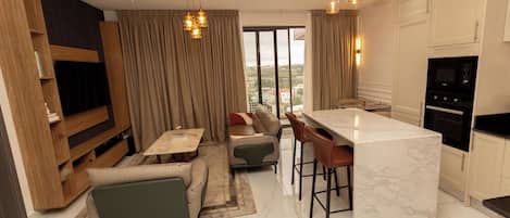 A modern living room with a sofa, a dining area, and a kitchen with a marble island.