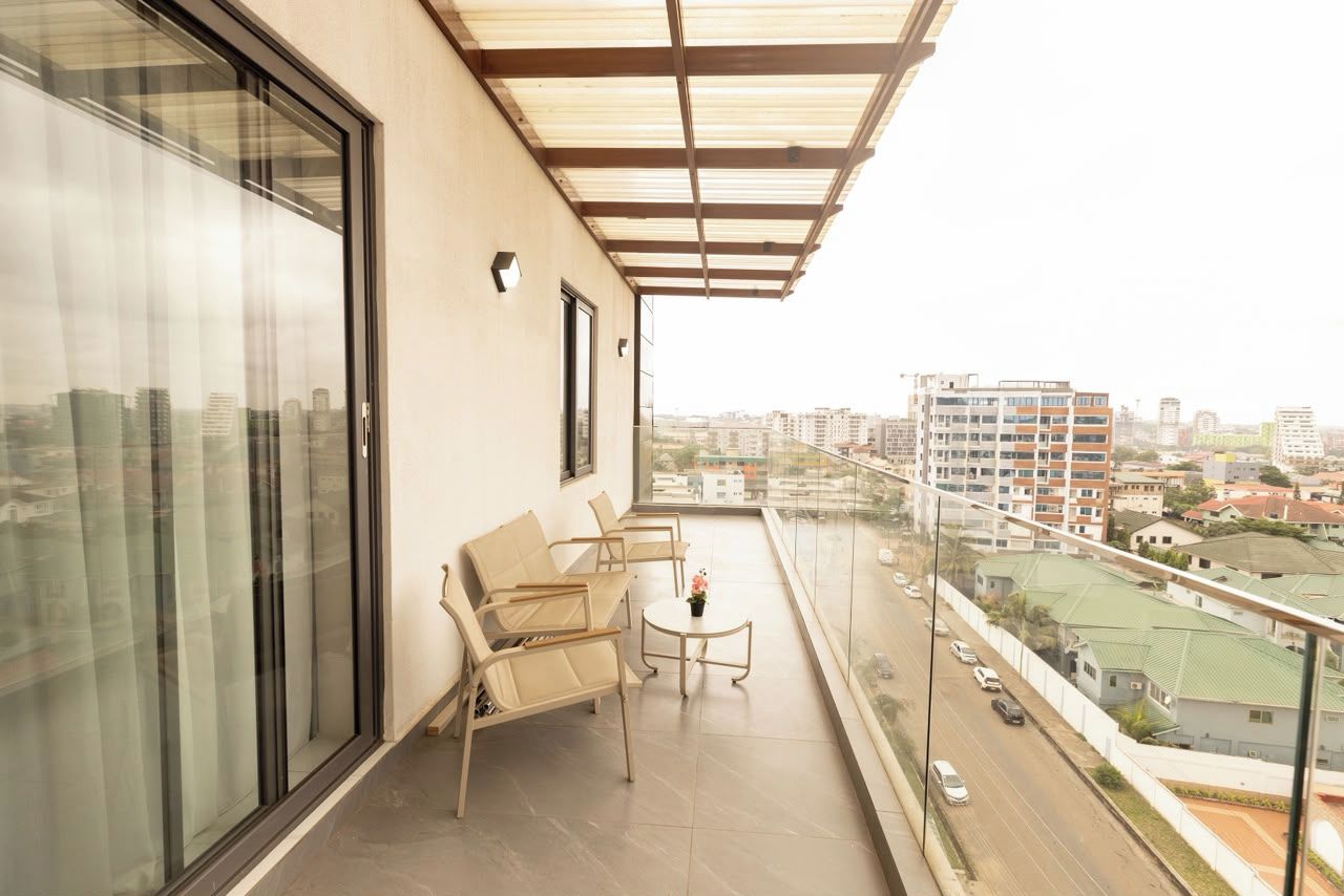 Varanda com vista para a cidade, porta de vidro e área de estar com mesa e cadeiras.