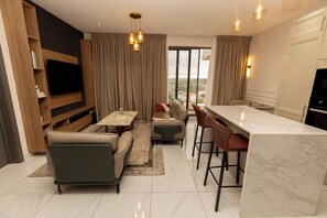 Uma sala de estar moderna com televisão de tela plana, um sofá, uma mesa de centro e um espaço de jantar com banquetas.