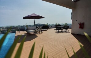 Eine Dachterrasse mit Pool, Liegestühlen, einem Tisch und einem Sonnenschirm.