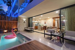 A modern outdoor living area with a pool, seating, and a kitchen visible through a glass partition. - Calakmul: Intimate 2BR w/ Private Plunge (Tulum)