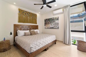 A bedroom with a bed, a ceiling fan, an air conditioning unit, a wall-mounted artwork, and a window with curtains. - Calakmul: Intimate 2BR w/ Private Plunge (Tulum)