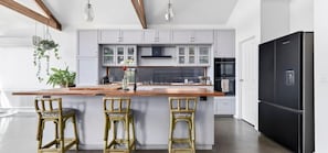 A modern kitchen with white cabinets, a black refrigerator, and a wooden island with bar stools. - Modern Heritage Retreat – walk to Pako & Waterfront (Greater Geelong)