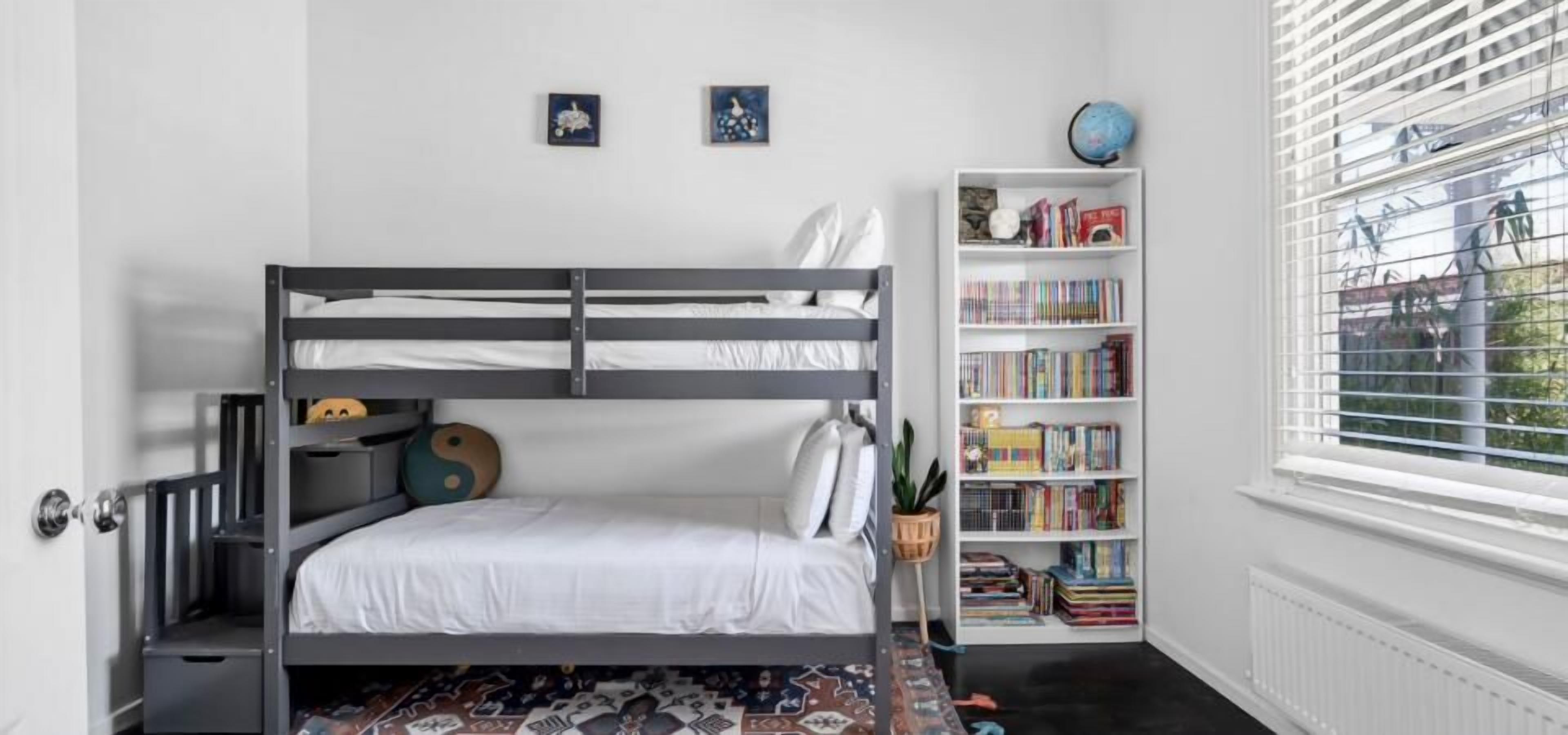 Een stapelbed met een boekenplank en een raam met jaloezieën.