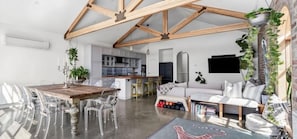 A spacious living area with a wooden ceiling, a dining table with chairs, a sofa, and a TV mounted on the wall. - Modern Heritage Retreat – walk to Pako & Waterfront (Greater Geelong)