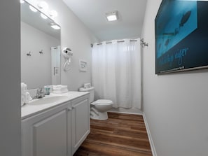Een badkamer met een wit wastafelmeubel, een haardroger, een toilet en een douchegordijn.