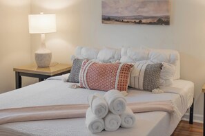 Una cama bien hecha con toallas enrolladas, una lámpara y un cuadro en la pared.