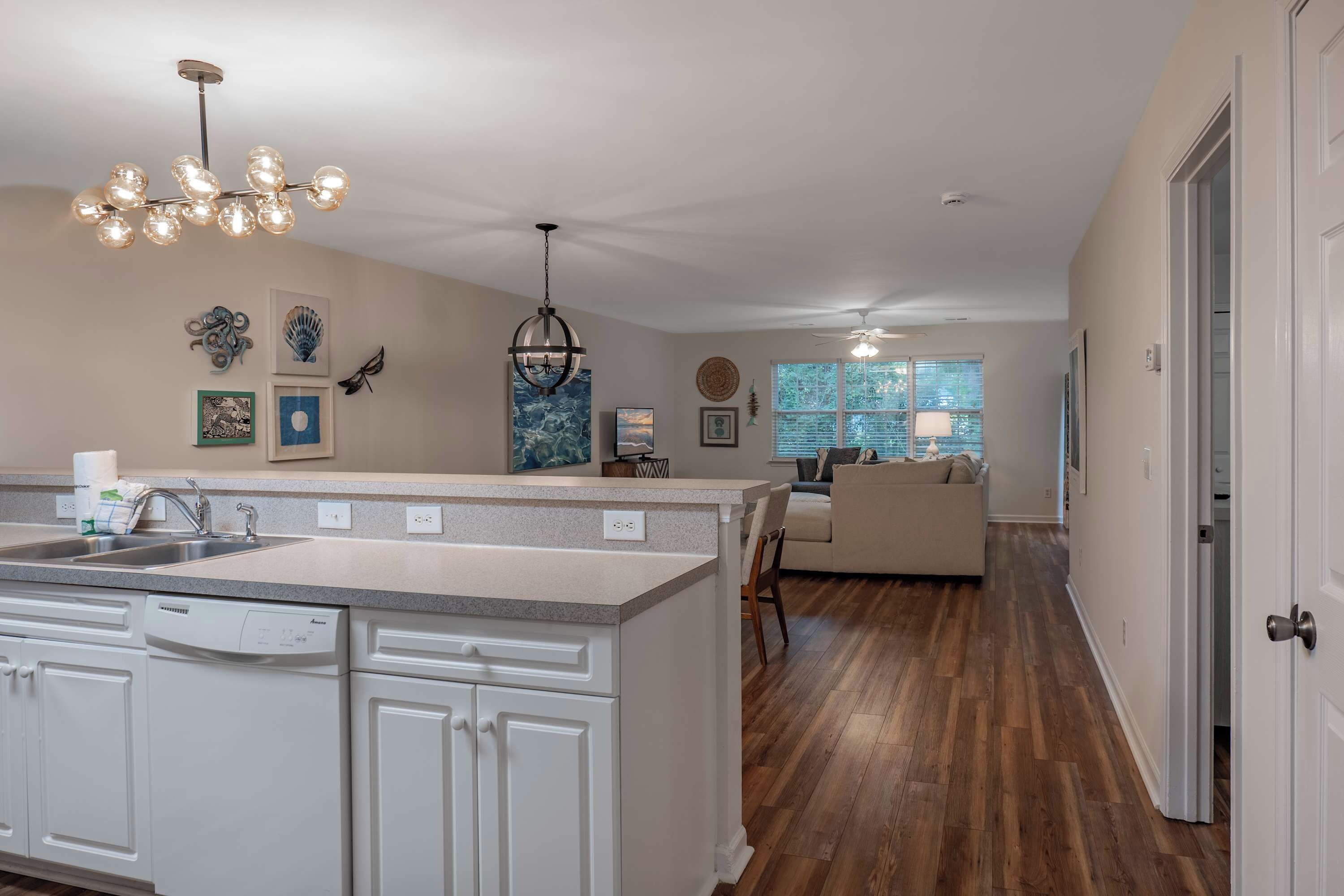 A modern kitchen with a central island, a dining area with a sofa, and a hallway leading to a door.