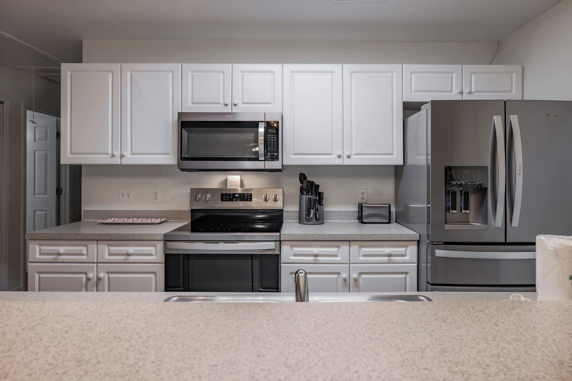 A modern kitchen with white cabinetry, a built-in microwave, a stainless steel refrigerator, and a stove.