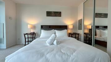 A hotel room with a large bed, two bedside tables, a nightstand, a painting on the wall, and a mirror.