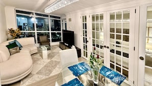 A modern living room with a sofa, coffee table, and a TV. There is a large window with a city view and a chandelier. - StayToronto - Union Station & Waterfront (Toronto)