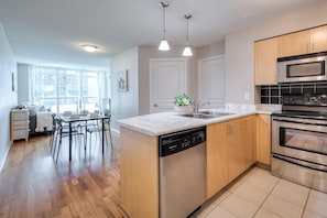 A modern kitchen with a dishwasher, double oven, and a dining area with a table and chairs. - StayToronto - Union Station & Waterfront (Toronto)
