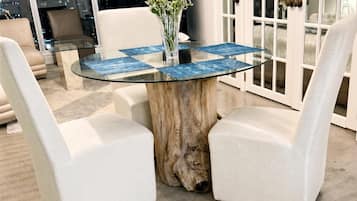 A round glass table with a wooden base, surrounded by two white upholstered chairs.
