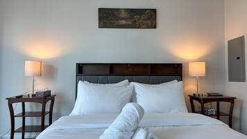 A neatly made bed with white linens, two bedside tables with lamps, and a painting above the bed.