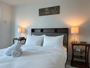 A hotel room with a neatly made bed, two bedside lamps, a painting above the bed, and a wooden nightstand with a tissue box. - StayToronto - Union Station & Waterfront (Toronto)