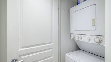 A white door with a silver handle, a white washing machine, and a white dryer stacked above it.