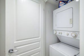 A white door with a silver handle, a white washing machine, and a white dryer stacked above it. - StayToronto - Union Station & Waterfront (Toronto)