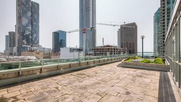 A rooftop terrace with a view of high-rise buildings, a construction crane, and a body of water.