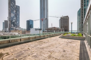 Une terrasse sur le toit offrant une vue sur des immeubles de grande hauteur, une grue de chantier et une étendue d’eau.