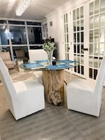Un comedor con mesa de vidrio, sillas blancas y un jarrón con flores.