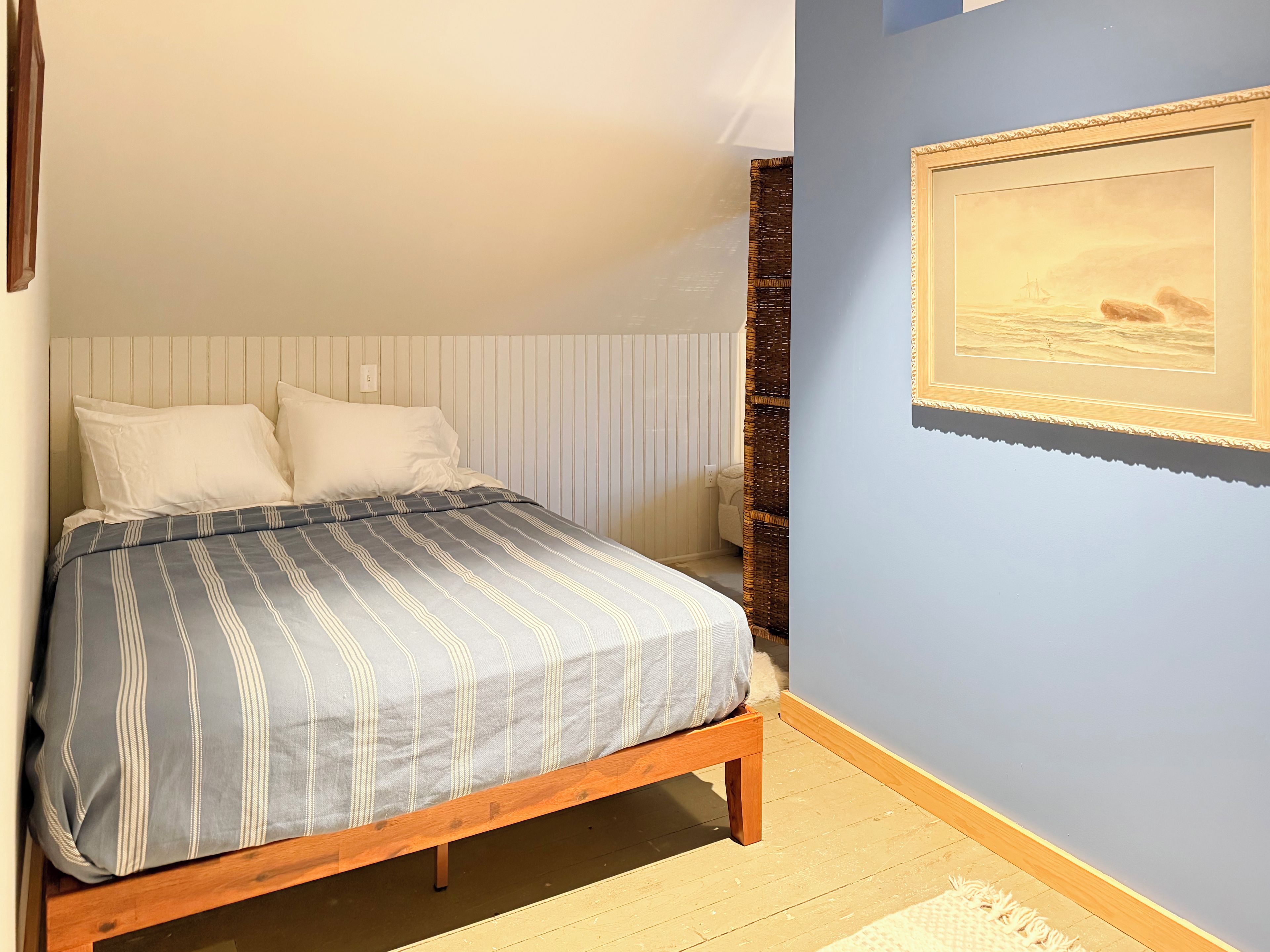 Un dormitorio con cama, un cuadro en la pared y suelo de madera.