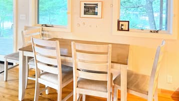 A dining area with a wooden table and chairs, framed pictures on the wall, and large windows.