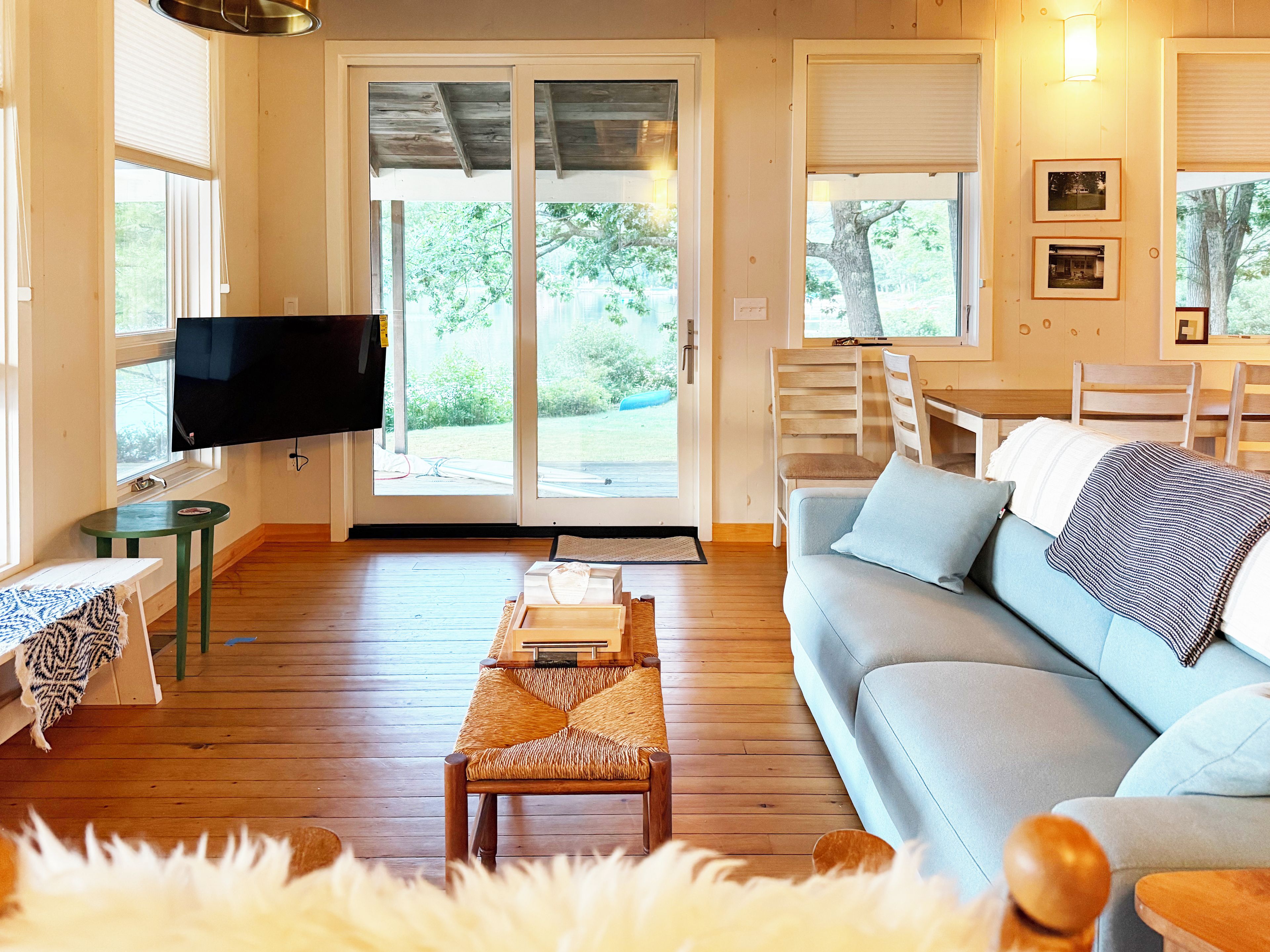 A living room with a sofa, a television, a dining table, and a view of the outdoors.