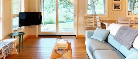 Un salon comprenant un canapé, un téléviseur, une table à manger et donnant sur l’extérieur.