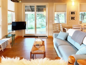 A living room with a sofa, a television, a dining table, and a view of the outdoors.