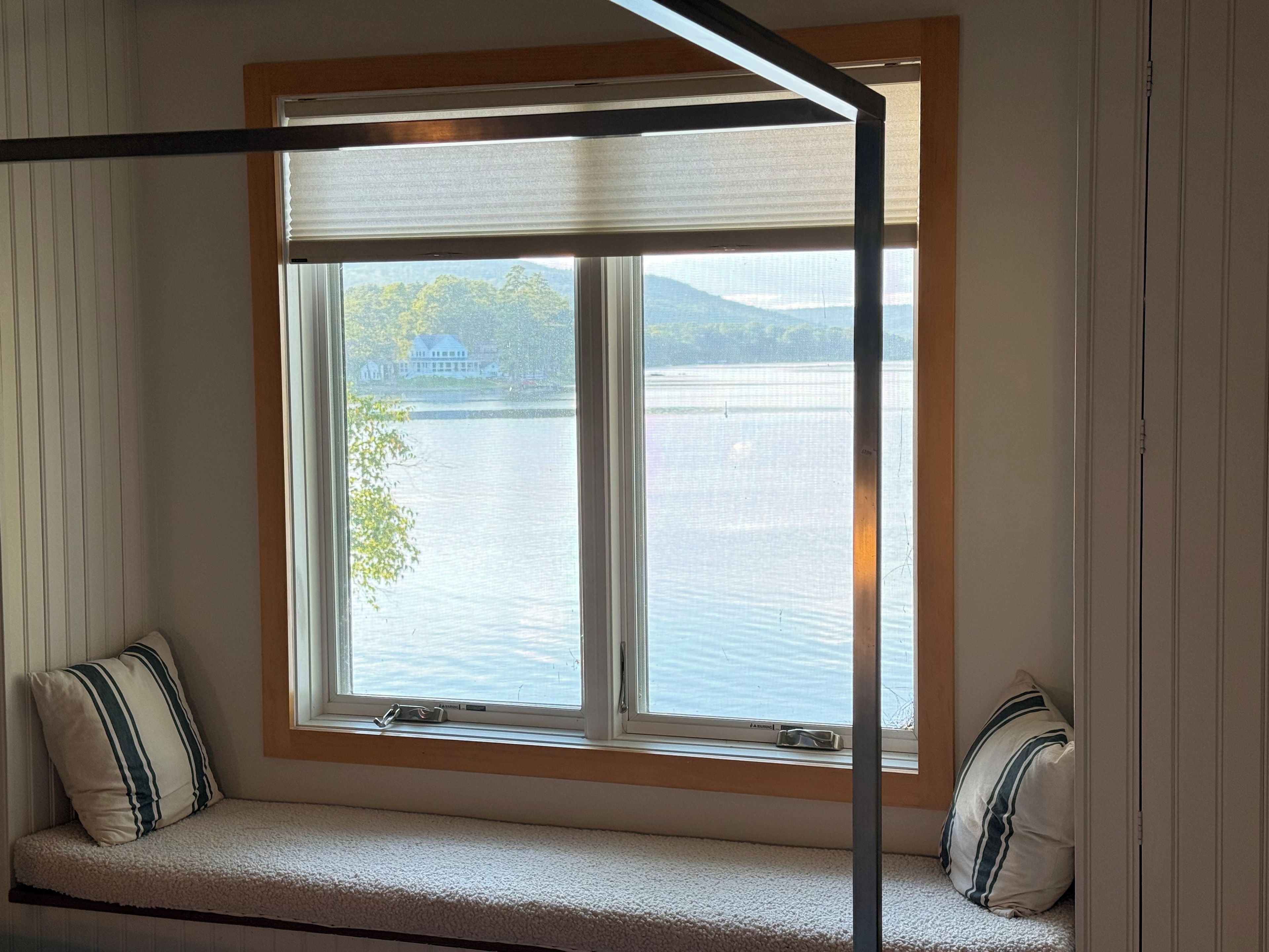 A room with a window overlooking a body of water and a distant house.