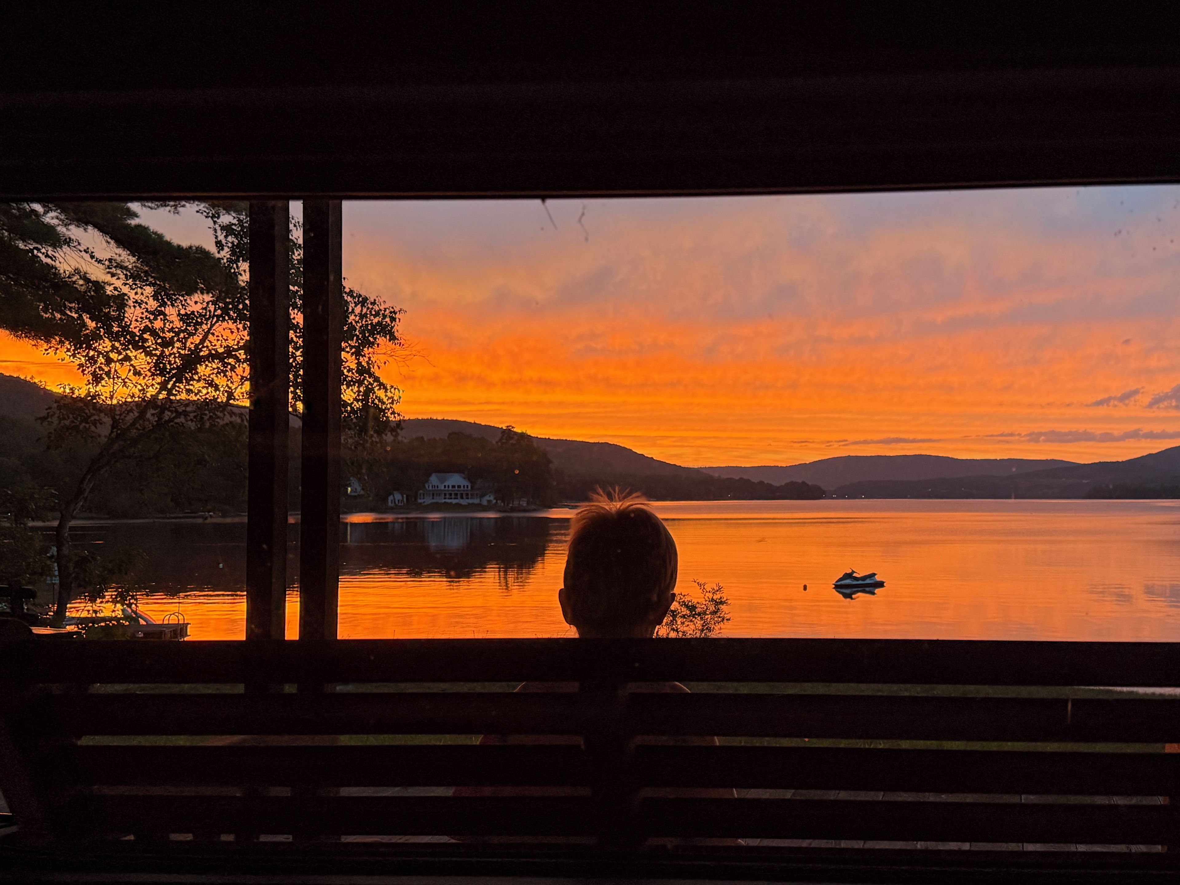 Une personne assise sur un banc, face à un lac, et contemplant le coucher de soleil.