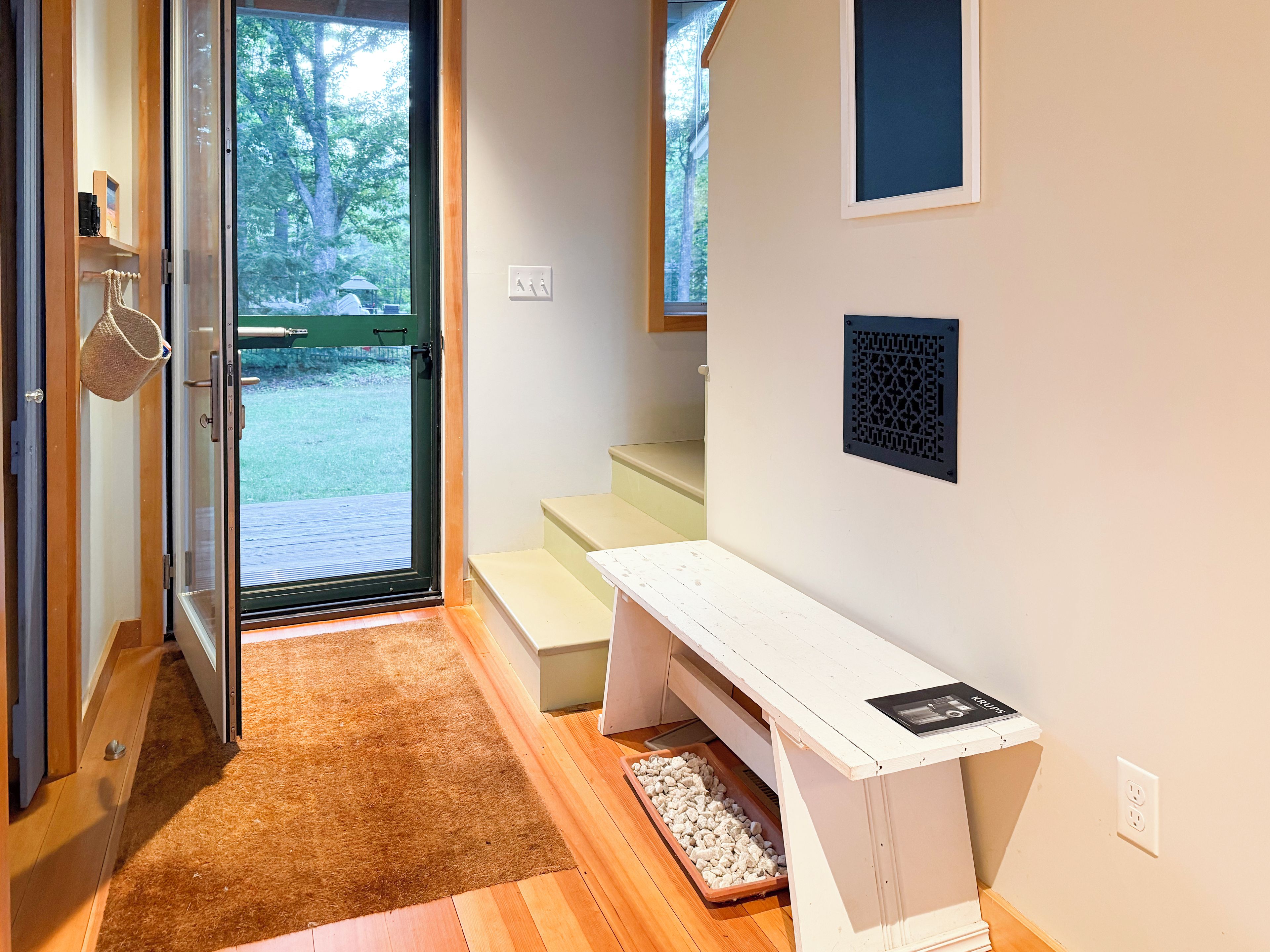 A modern interior with a wooden floor, a white bench, and a door leading to an outdoor area.