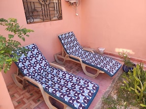 Two sun loungers with geometric patterned cushions, a potted plant, and a window with a metal grill. - Charming Villa in Marrakesh with a garden and a swimming pool (Marrakesh)