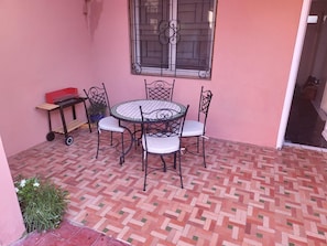 A patio with a round table and four chairs, a small table with a red box, and a window with decorative metal bars. - Charming Villa in Marrakesh with a garden and a swimming pool (Marrakesh)