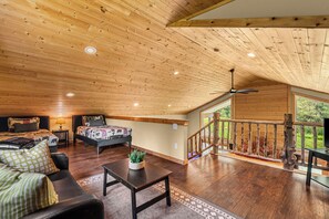 A spacious living area with a high ceiling, a bed, a sofa, a coffee table, and a staircase leading to an outdoor deck. - Nature's Acres | Private Hot Tub, Pond & Gazebo (Leavenworth)